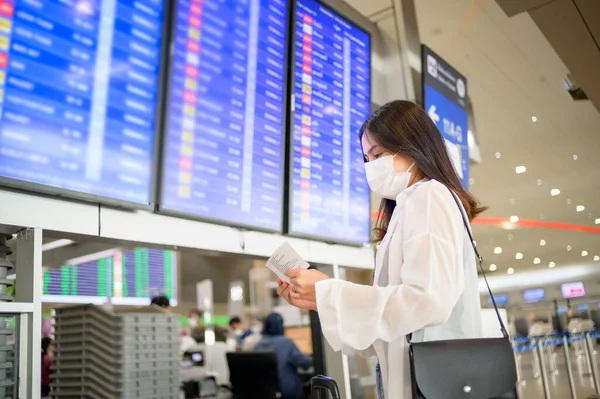 A traveller woman is wearing protective mask in International airport, travel under Covid-19 pandemic, safety travels, social distancing protocol, New normal travel concept .