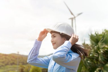 Female engineer working on the seaside wearing a protective helmet over electrical turbines background.	