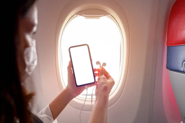 Close up woman hand holding smartphone over window aircraft background , transportation technology concept