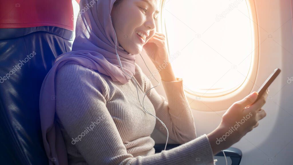 A Young muslim woman wearing hijab using smartphone onboard, travel and holidays concept