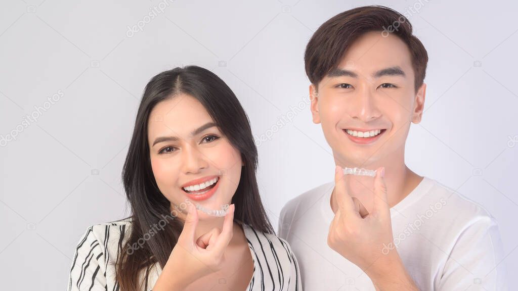 Young smiling man amd woman holding invisalign braces over white background studio, dental healthcare and Orthodontic concept.