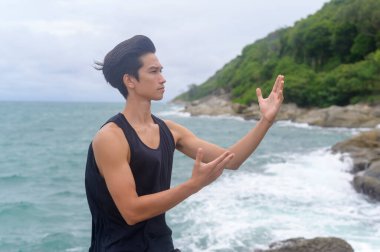 Spor giyimli genç adam dövüş sanatları yapıyor, Qigong, Tai Chi deniz kenarındaki kayada, sağlık ve meditasyon konsepti. 