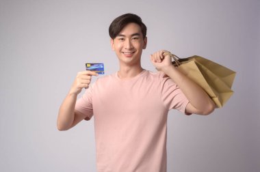 A Young asian man holding credit card and shopping bag over white background studio, shopping and finance concept.