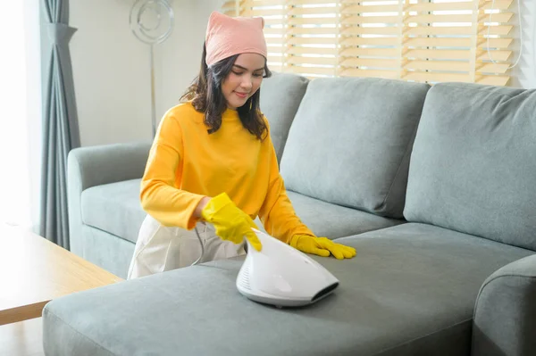 Young happy woman wearing yellow gloves  and vacuum Cleaning a sofa in living room.