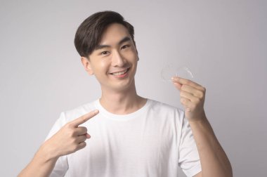 Elinde gülümseyen genç bir adam beyaz arka plan stüdyosu, diş sağlığı hizmetleri ve ortodontik konsept üzerinde diş teli takıyor..