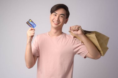 A Young asian man holding credit card and shopping bag over white background studio, shopping and finance concept.