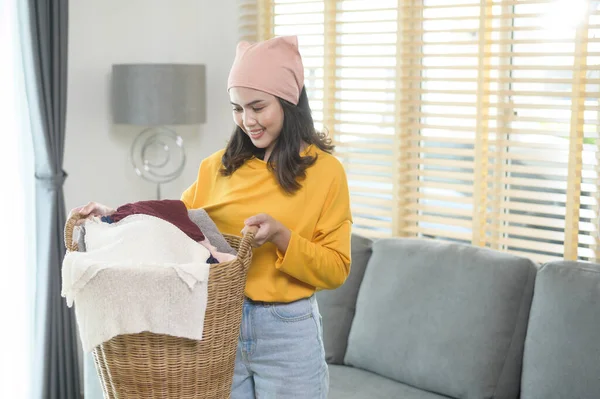 Young happy woman wearing yellow shirt holding a basket full of clothes at home, laundry concept