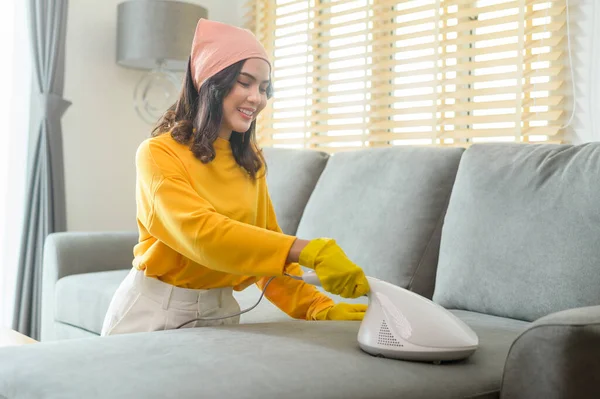 Young happy woman wearing yellow gloves  and vacuum Cleaning a sofa in living room.