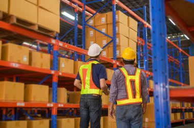 A Group of young worker wearing helmet checking inventory and discussing in modern warehouse.