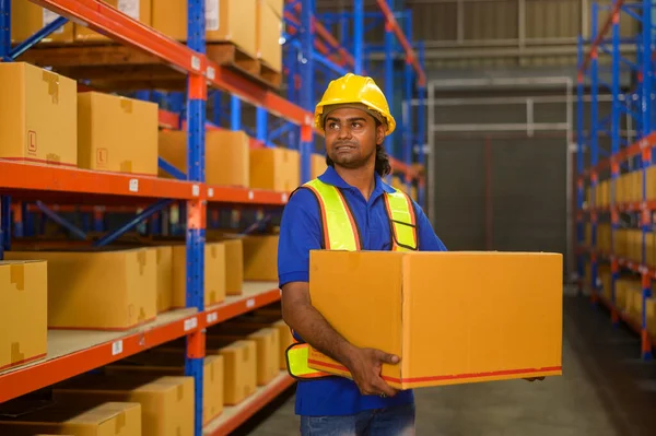 A Young mixed race male worker wearing helmet lifting cardboard box in warehouse, machinery and Logistics concept.