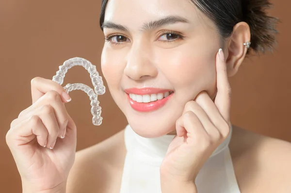 Güzel dişleri olan genç bir kadın Invisalign, sağlıklı diş konseptini elinde tutuyor. 