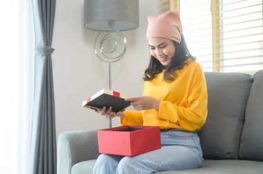A Young surprised woman opening a gift box in living room.