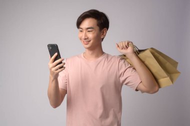A Young asian man holding smartphone and shopping bag over white background studio, shopping and finance concept.