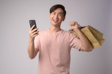 A Young asian man holding smartphone and shopping bag over white background studio, shopping and finance concept.