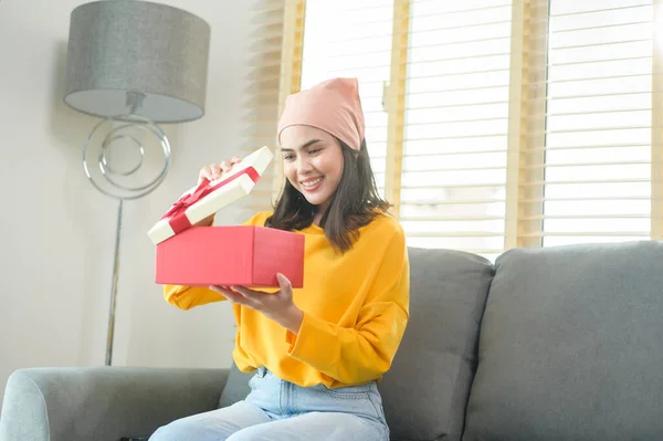 A Young surprised woman opening a gift box in living room.