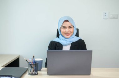 A Young muslim business woman working on laptop with documents in modern office