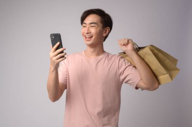 A Young asian man holding smartphone and shopping bag over white background studio, shopping and finance concept.