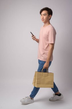 A Young asian man holding smartphone and shopping bag over white background studio, shopping and finance concept.