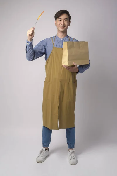 Portrait Young Asian Man Wearing Apron Holding Paper Bag Turner — Zdjęcie stockowe
