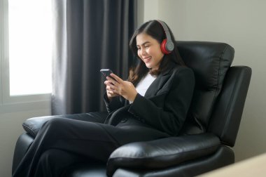 A Young relaxing business woman using smartphone and listening to music in modern office.