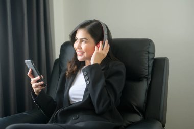A Young relaxing business woman using smartphone and listening to music in modern office.