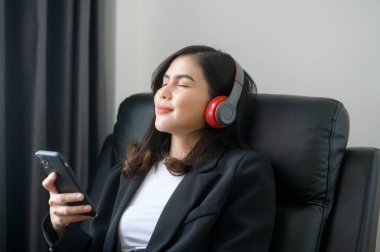 A Young relaxing business woman using smartphone and listening to music in modern office.