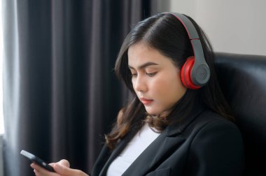A Young relaxing business woman using smartphone and listening to music in modern office.