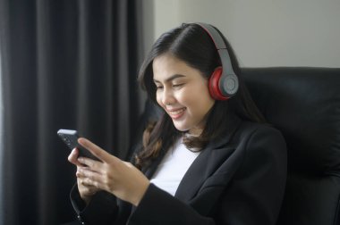 A Young relaxing business woman using smartphone and listening to music in modern office.