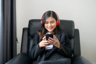 A Young relaxing business woman using smartphone and listening to music in modern office.