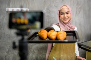 A Beautiful muslim woman is making bakery while live streaming or recording video on social media in her house, coffee shop business concept. 