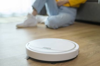 A Young happy woman using Robotic vacuum cleaner in living room 