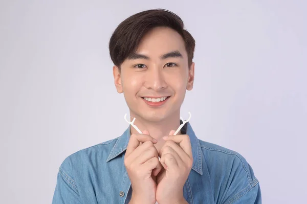 A Young smiling man holding dental floss over white background studio, dental healthcare and Orthodontic concept.