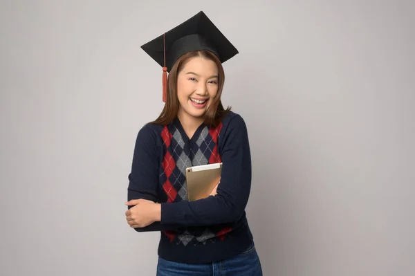 A Young smiling woman holding graduation hat, education and university concept