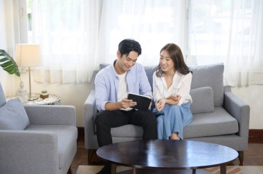 Evde tablet kullanan gülümseyen Asyalı genç bir çift. 