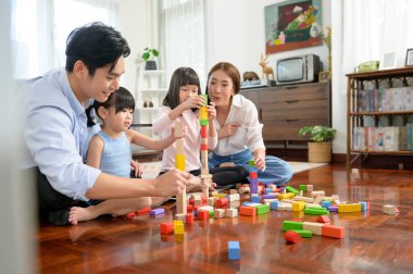 Çocuklarla oynayan ve renkli tahta bloklardan kule inşa eden Asyalı bir aile evdeki oturma odasında, eğitim oyununda.