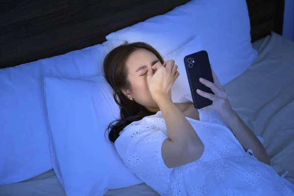 An asian woman feeling eye strain fatigue while using smartphone in bedroom