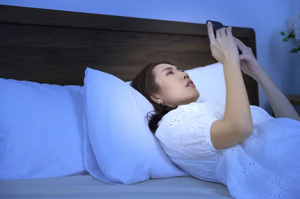 An asian woman feeling eye strain fatigue while using smartphone in bedroom