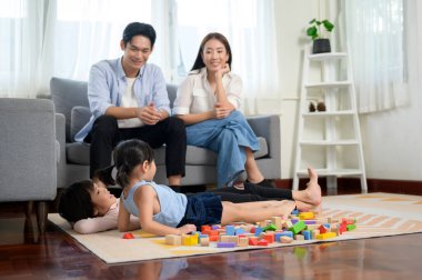 Çocuklarla oynayan ve renkli tahta bloklardan kule inşa eden Asyalı bir aile evdeki oturma odasında, eğitim oyununda.