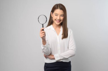 A Young asian woman holding magnifying glass over white background, analysis and finance concept. 	