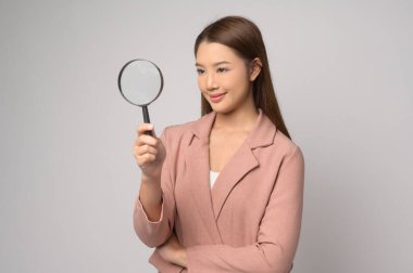 A Young asian woman holding magnifying glass over white background, analysis and finance concept. 	