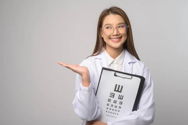 一位年轻的女眼科医生 戴着眼镜 在蓝色的背景画室上方挂着眼图 她的保健理念 — 图库照片