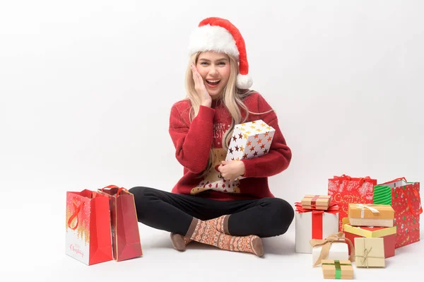 Portrait of happy Caucasian young woman in santa claus hat with gift box and shopping bags over white background