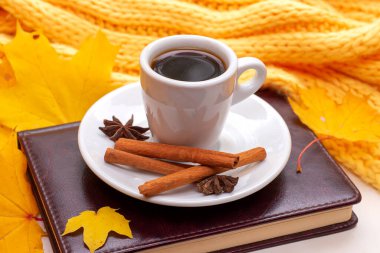 Üzerinde not defteri olan bir fincan kahve, ahşap bir masanın üzerinde kuru sarı yapraklar. Sonbahar havası.