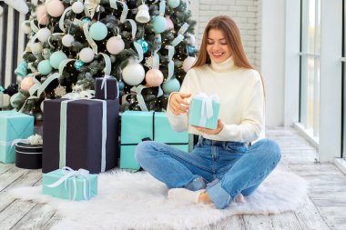 Noel hediyelerini süslenmiş bir Noel ağacının yanında açan genç bir kadın. Noel, Yeni Yıl Kutlama Konsepti.