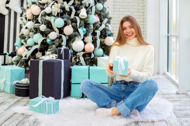 Noel hediyelerini süslenmiş bir Noel ağacının yanında açan genç bir kadın. Noel, Yeni Yıl Kutlama Konsepti.