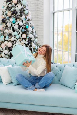 Noel ağacının yanında beyaz süveter giyen güzel bir kadın yeni yılı evde kutluyor.