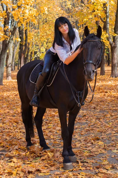Güzel, mutlu genç bir kadın sonbahar parkında atıyla yürüyor.