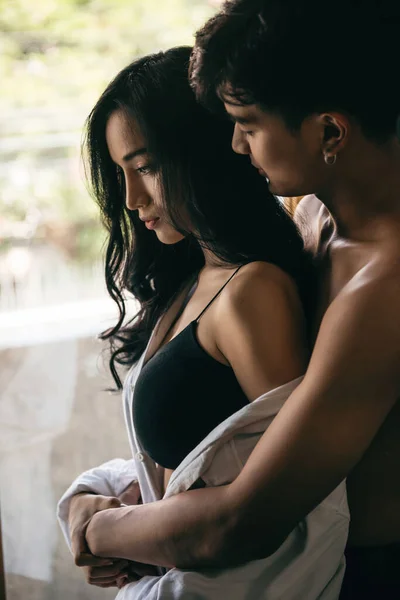 若いアジアの女性の黒い長い髪と彼女の男が寝室で問題を抱えていることを示す写真 窓の近くで抱擁し — ストック写真