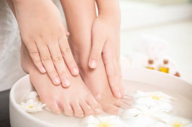 Kadının elini ve ayaklarını tabakta, tahta zeminde su ve çiçeklerle ıslattığı yakın çekim görüntüsü. Kadın ayakları ve el kaplıcası için spa ve ürün. Seramik kasede beyaz çiçekler.