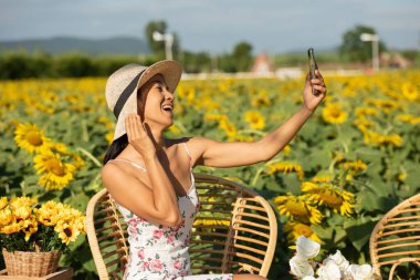 Asyalı kadınlar ayçiçeği tarlasıyla fotoğraf çekiyorlar, akıllı telefonları ellerinde tutuyorlar ve selfie çekiyorlar. hafta sonu konseptine göre seyahat.